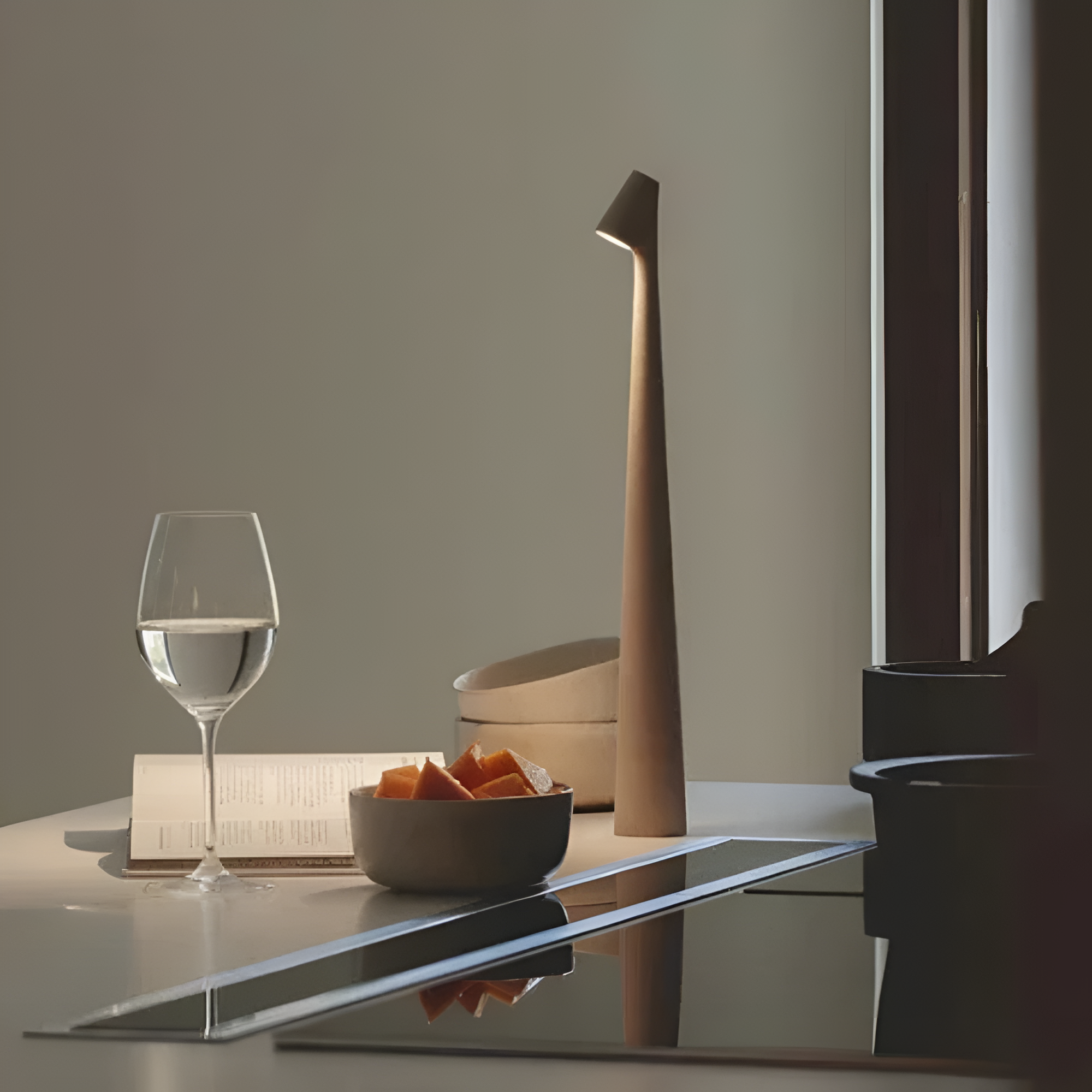 Modern kitchen setup with a wine glass, bowl of fruit, and decorative item on a reflective surface.