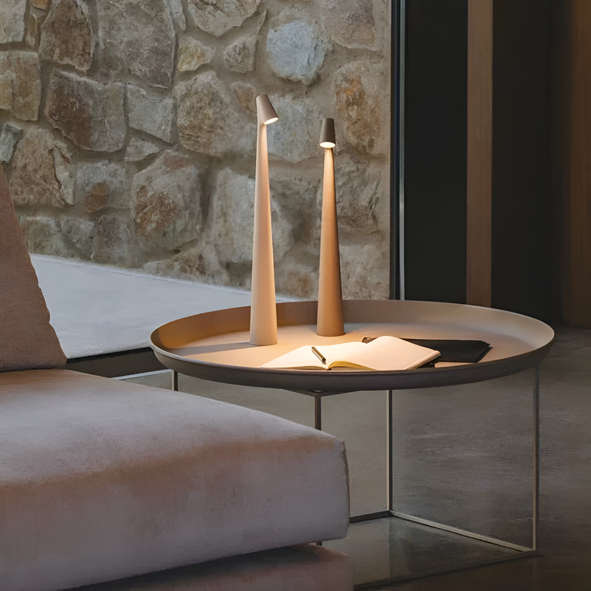 Modern side table with two tall, thin lamps against a stone wall.