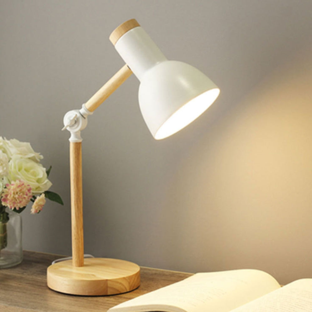 Table lamp with wooden base and white shade on a table next to flowers and an open book.