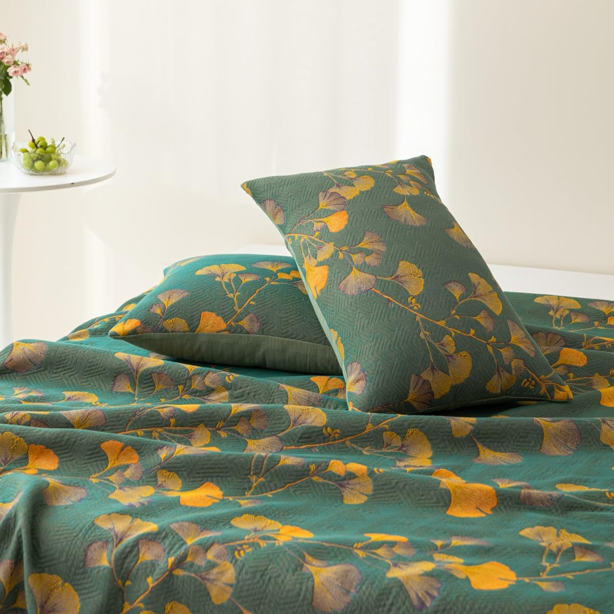 Floral patterned bedspread and pillows on a bed with a white curtain in the background.
