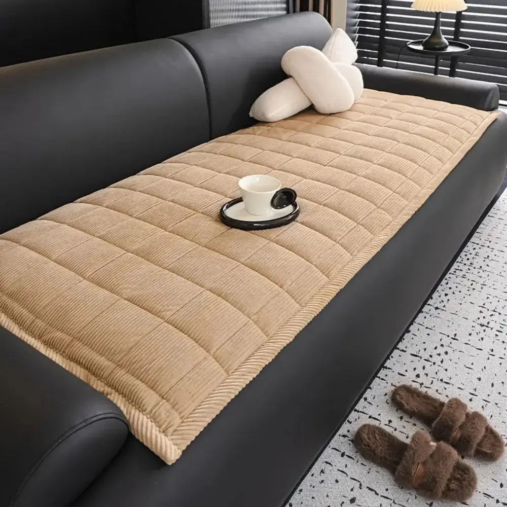 Beige quilted sofa cover on a black sofa with a cup and saucer on a small table.