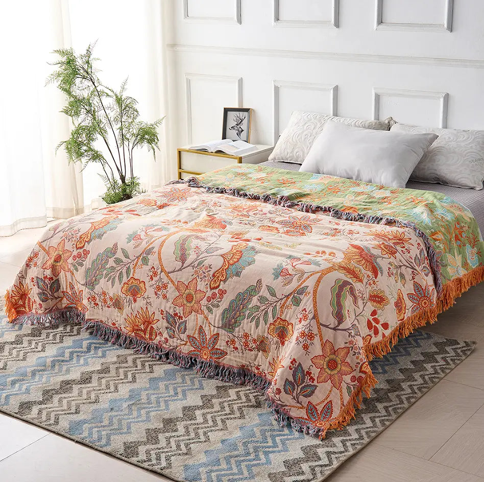 Decorative floral quilt on a bed in a bright bedroom with a plant and books.