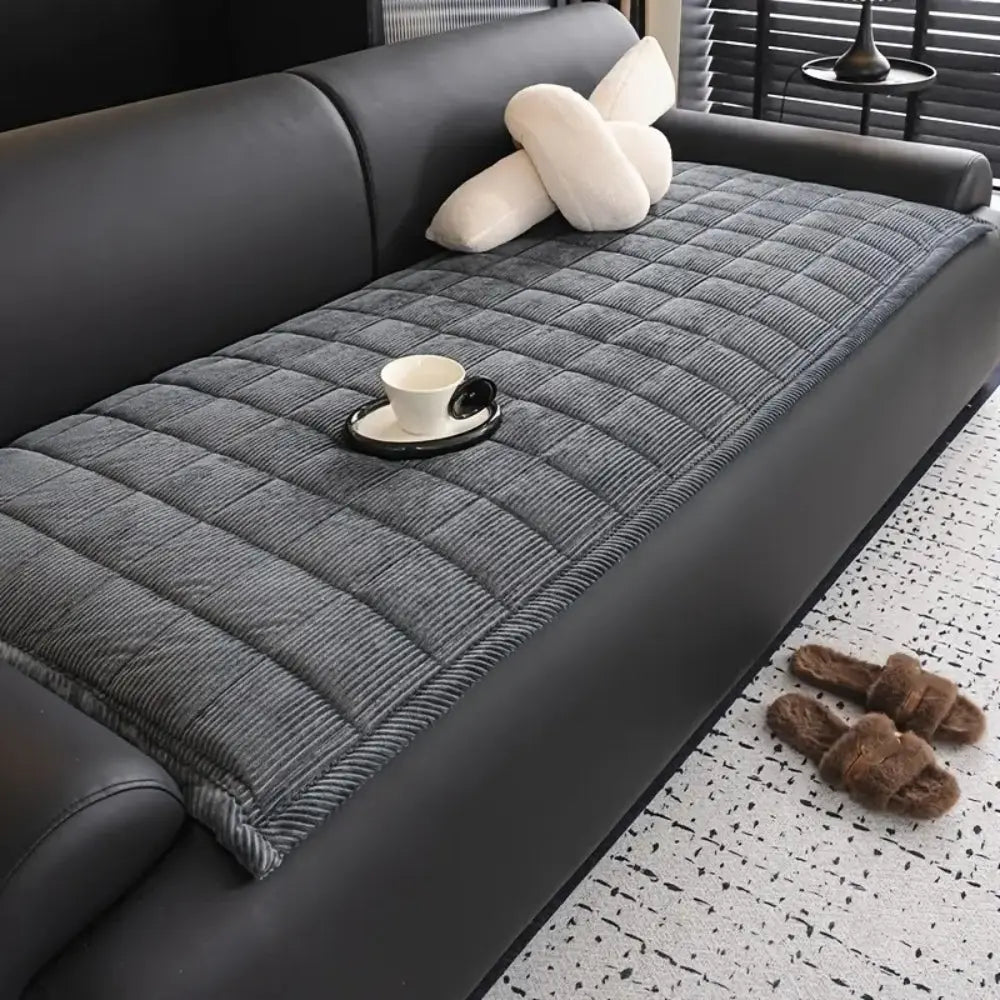 Gray quilted sofa cover on a black sofa with a cup and saucer on a small table.