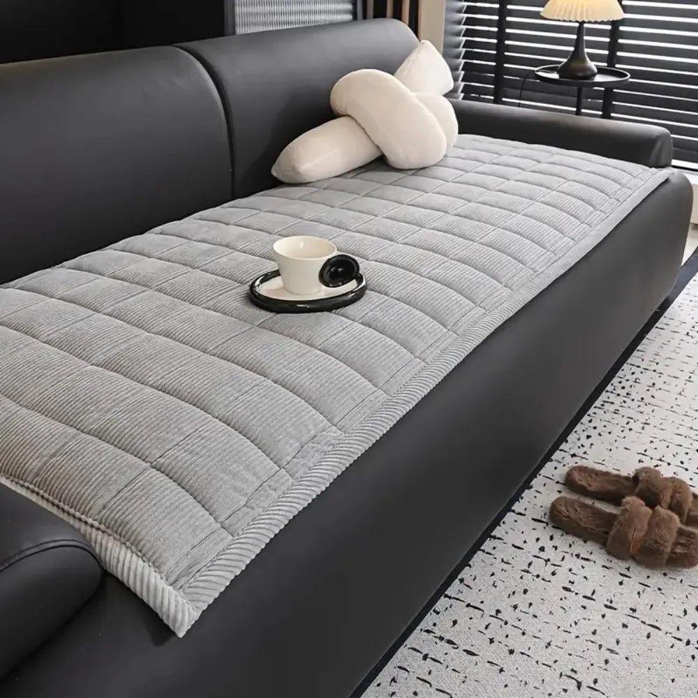 Gray quilted sofa cover on a black sofa with a cup and saucer on a small table.