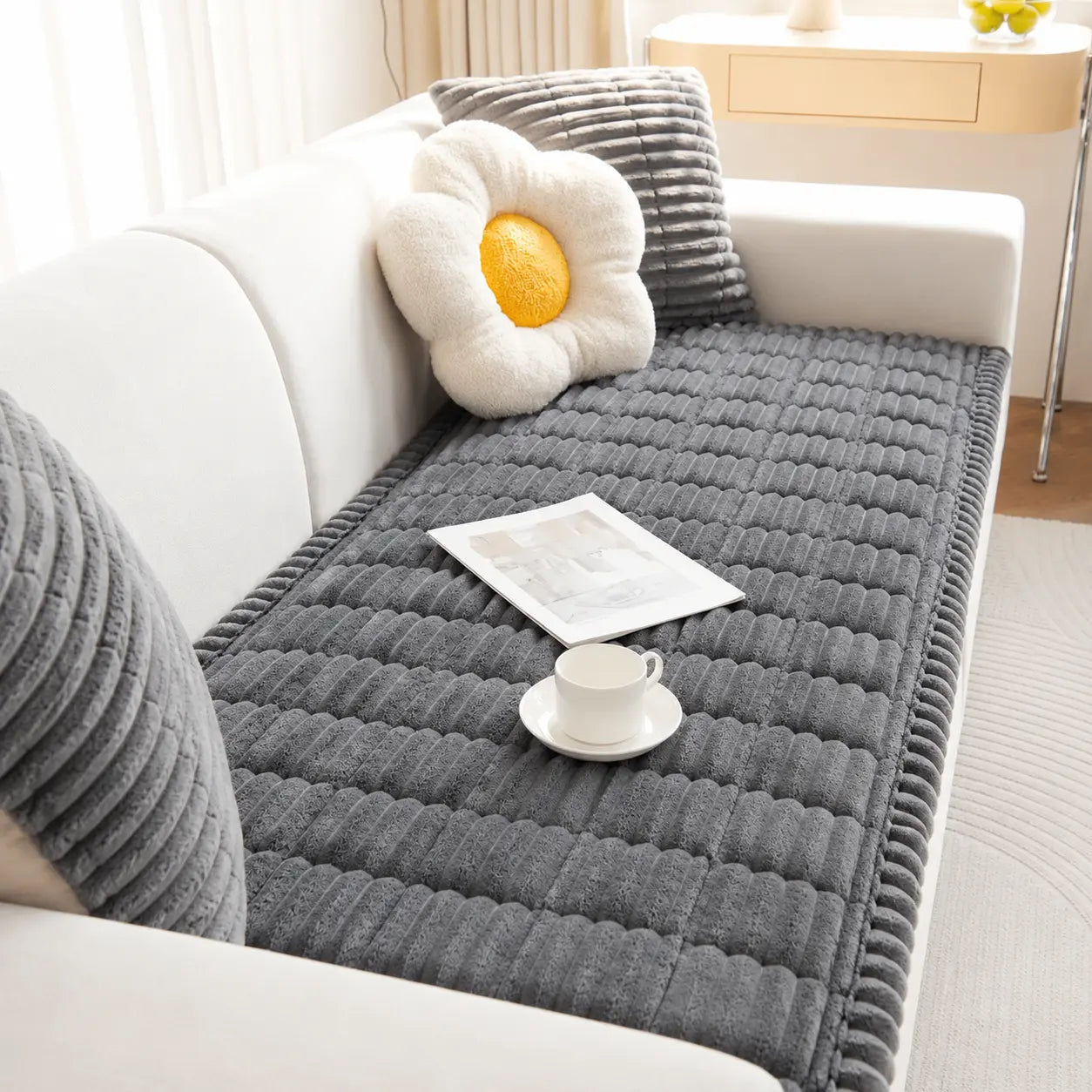 Gray textured rug on a white sofa with a cup and saucer, newspaper, and decorative pillow.
