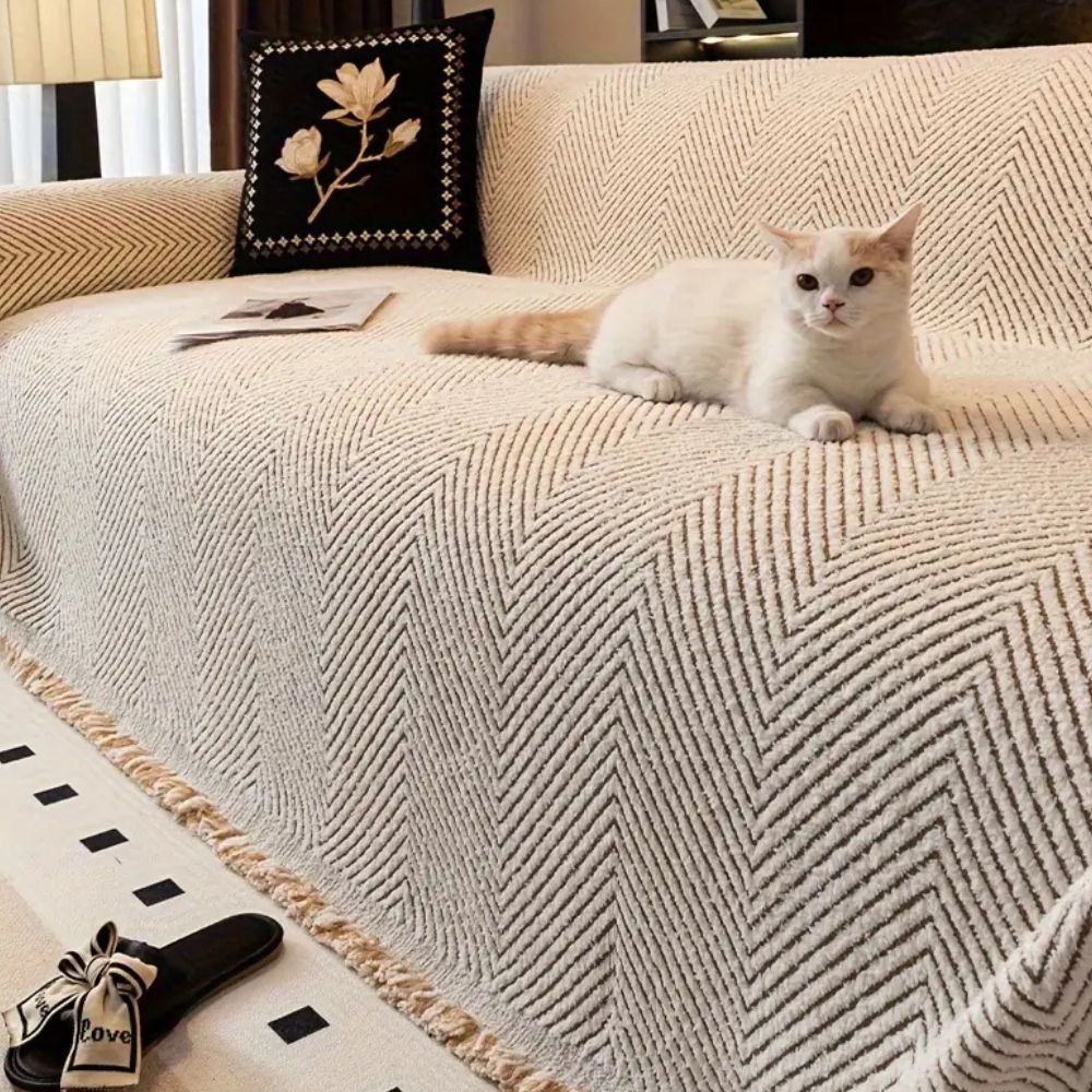 White cat sitting on a textured beige sofa with a decorative pillow.