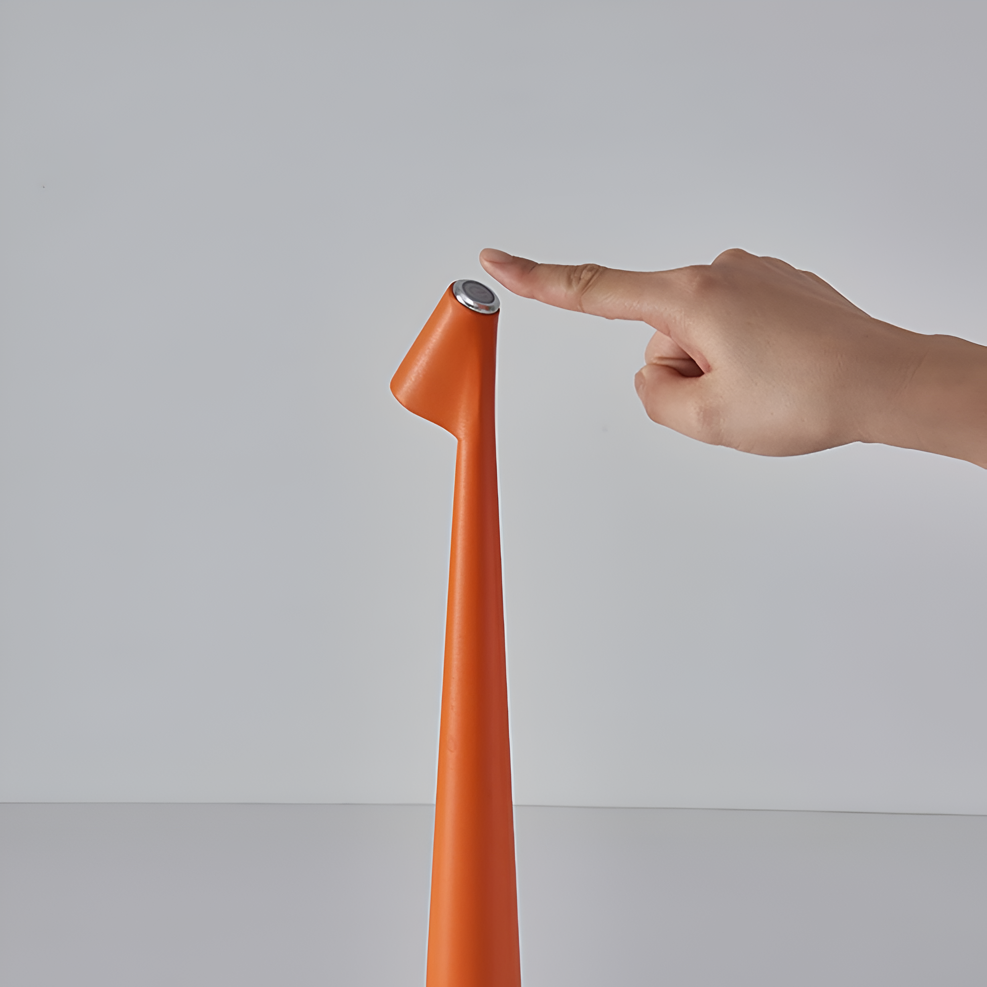 Hand pointing to an orange cylindrical object with a silver top on a gray background