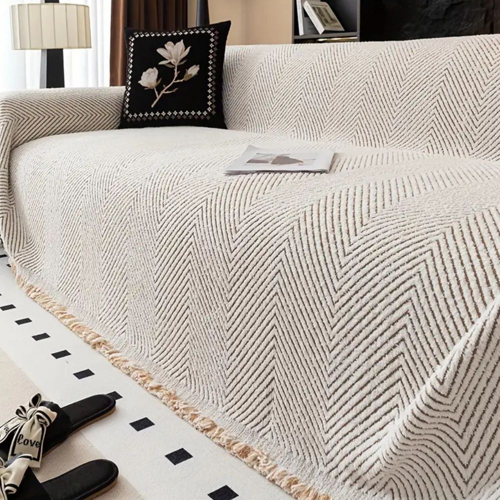 Beige textured throw blanket on a sofa with decorative pillows and a lamp in the background.