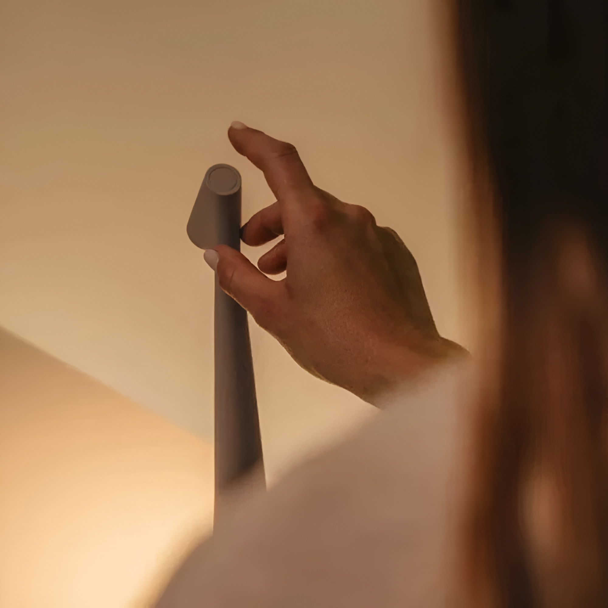Hand adjusting a lampshade on a lamp with a warm glow.