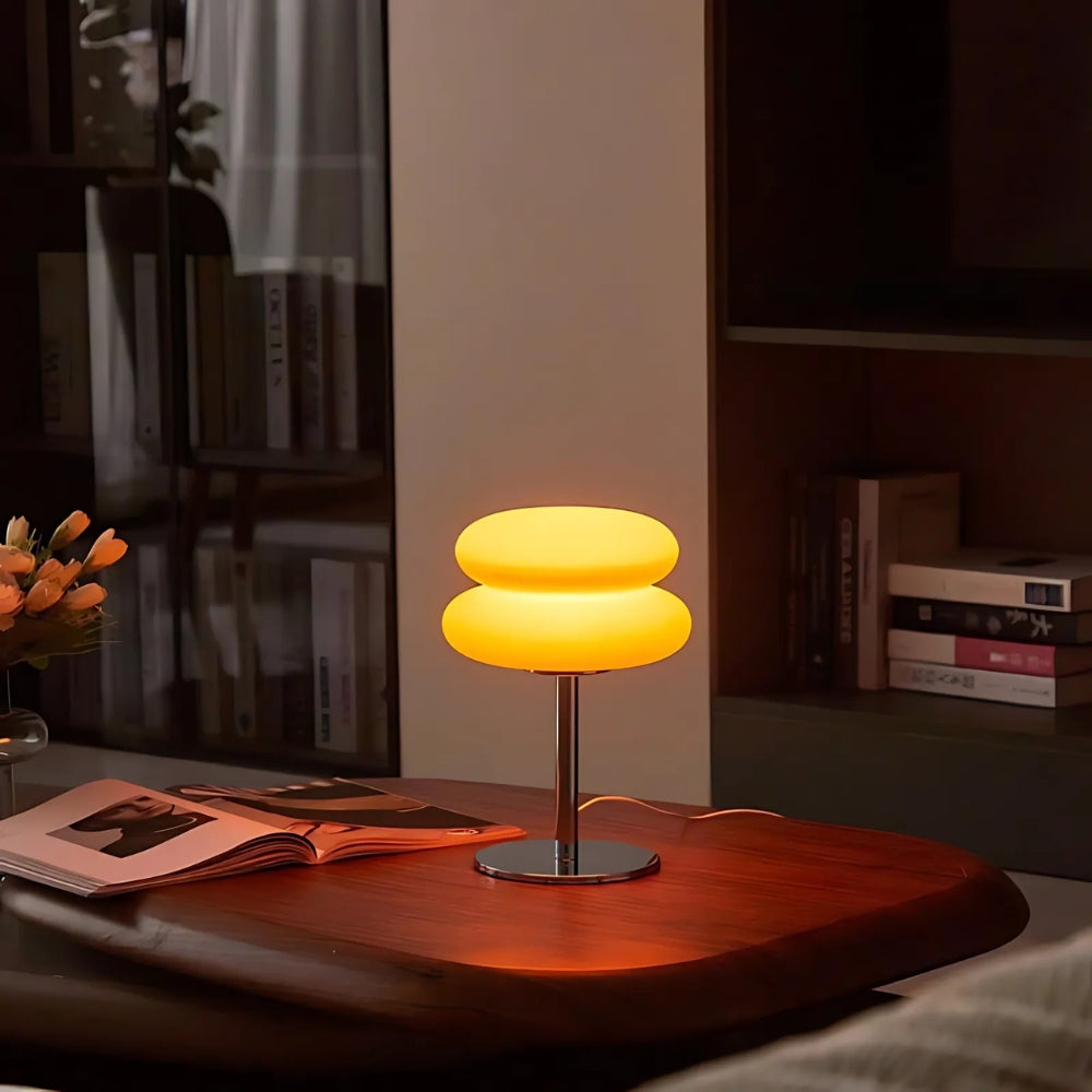 Modern table lamp with a warm glow on a wooden surface in a dimly lit room.