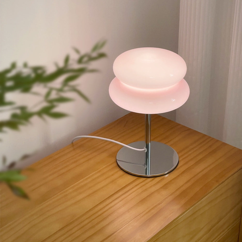 Pink table lamp on a wooden surface with a plant in the background