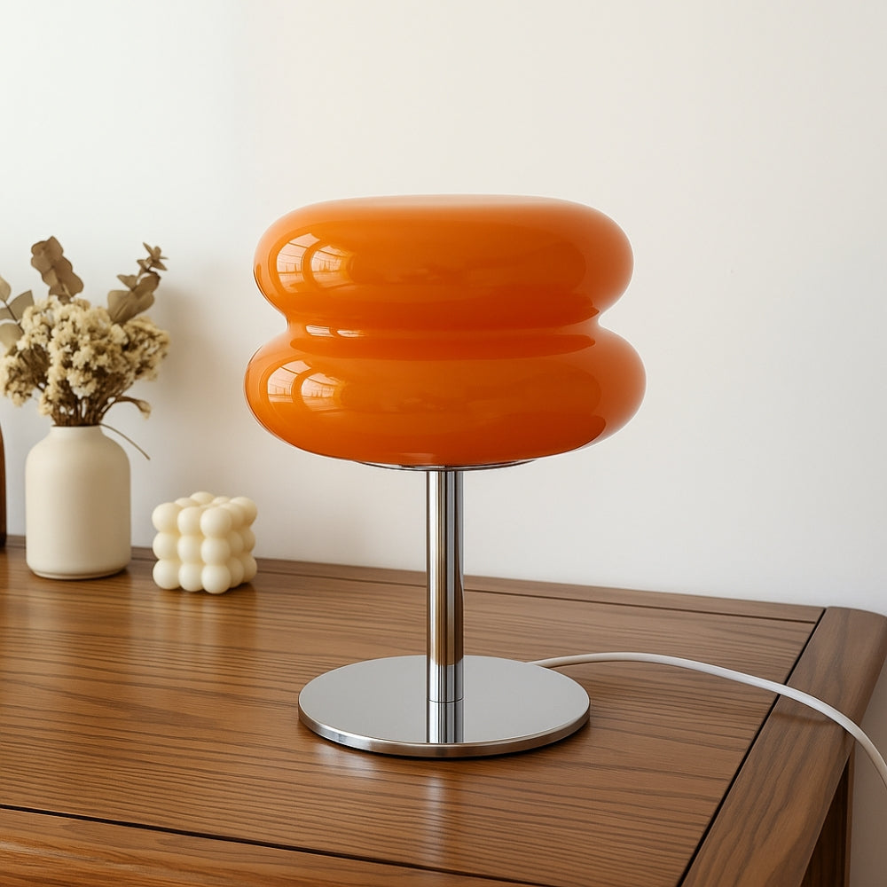 Orange table lamp with a metallic base on a wooden surface, with decorative items in the background.