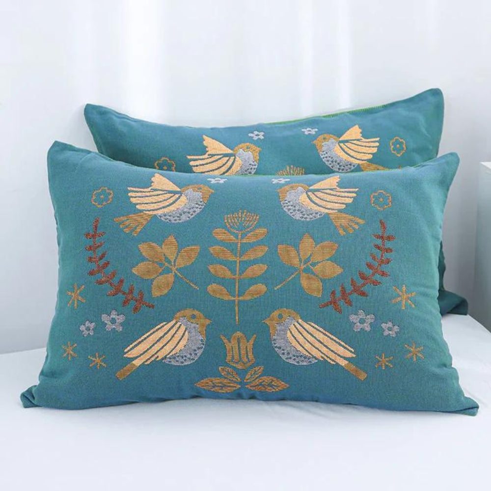 Two decorative pillows with bird and leaf patterns on a white surface.