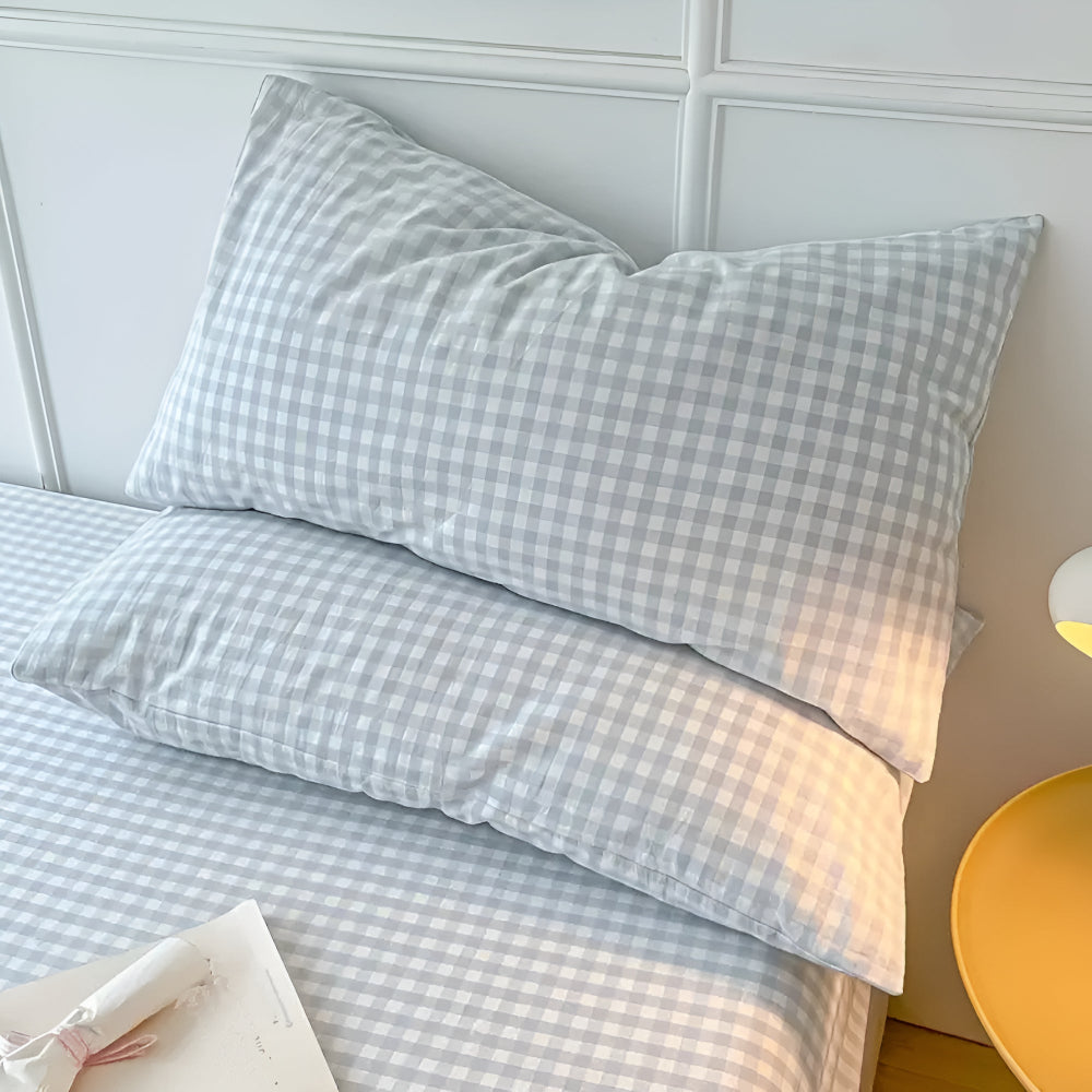 Checkered bed sheets and pillows on a bed with a white paneled wall in the background.