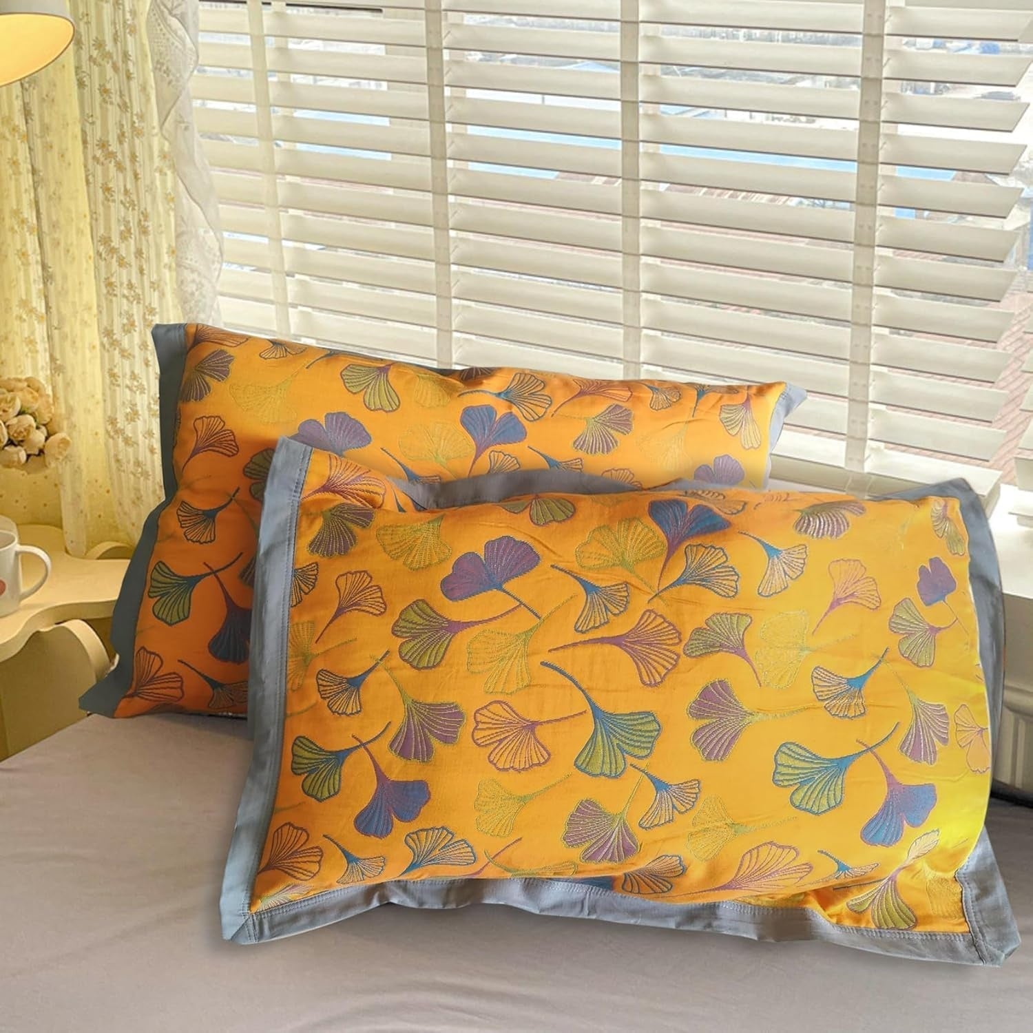 Decorative pillows with a floral pattern on a bed in a room with light filtering through blinds.