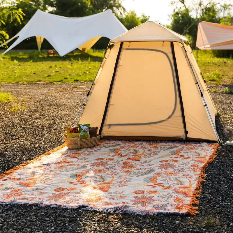 Beige tent with a colorful rug and basket on a gravel surface with greenery in the background
