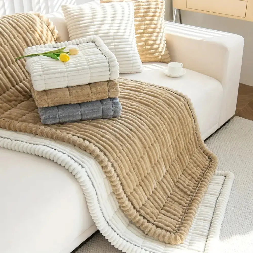 Beige textured blanket draped over a white sofa with cushions in a cozy living room.