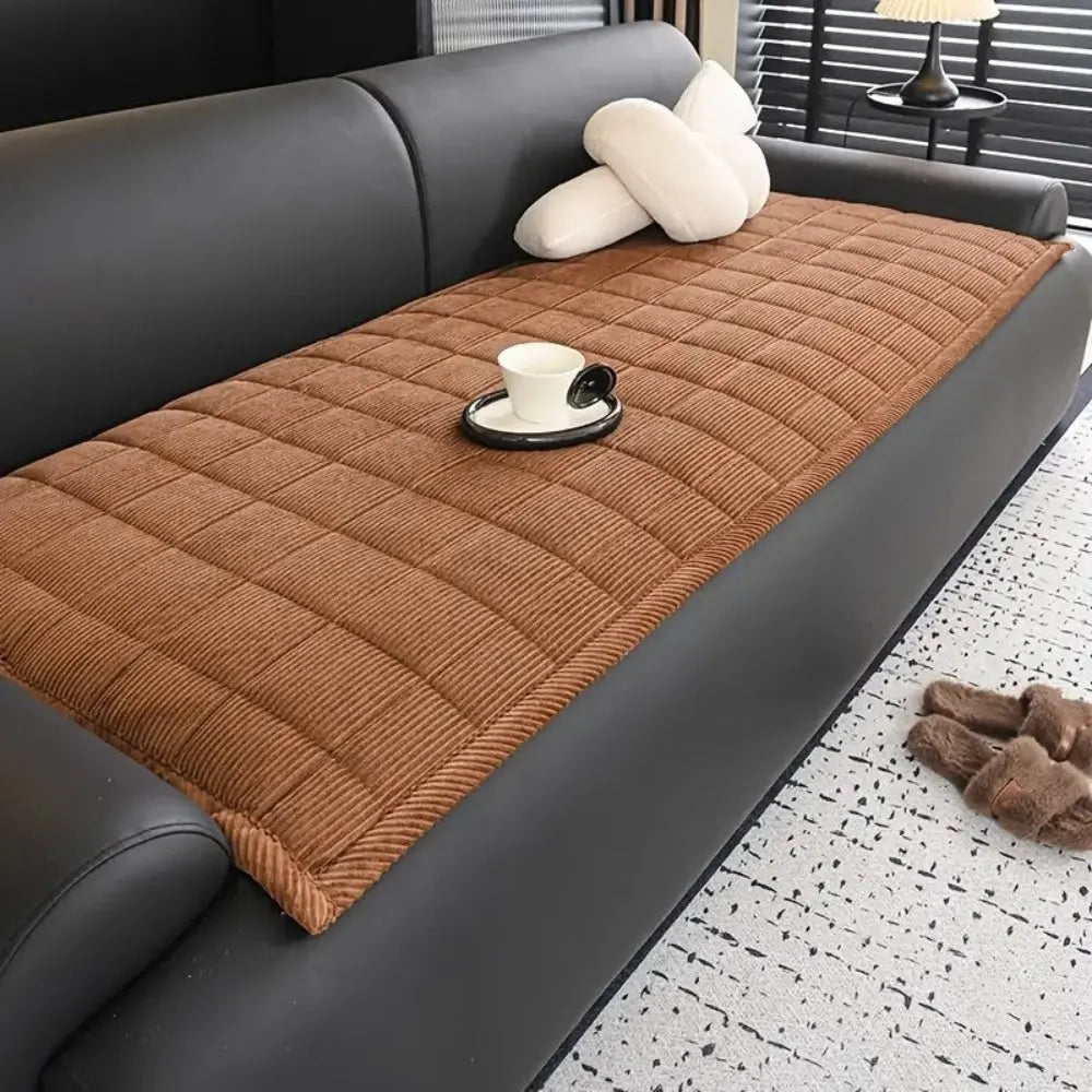 Brown quilted sofa cover on a gray sofa with a cup and saucer on a black coaster.