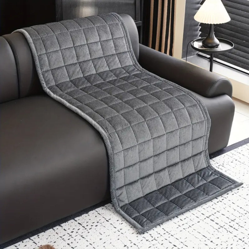 Gray quilted throw blanket draped over a brown sofa in a living room.