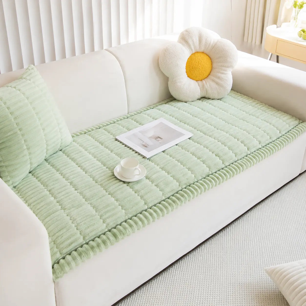 Green quilted sofa cover on a white sofa with decorative pillows in a living room setting.