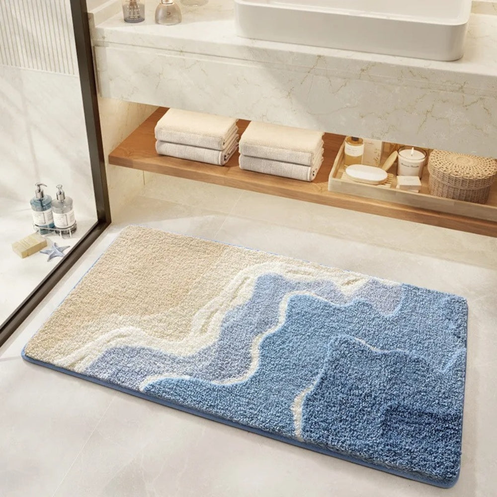Bath mat with blue and beige design on a bathroom floor, with towels and toiletries in the background.